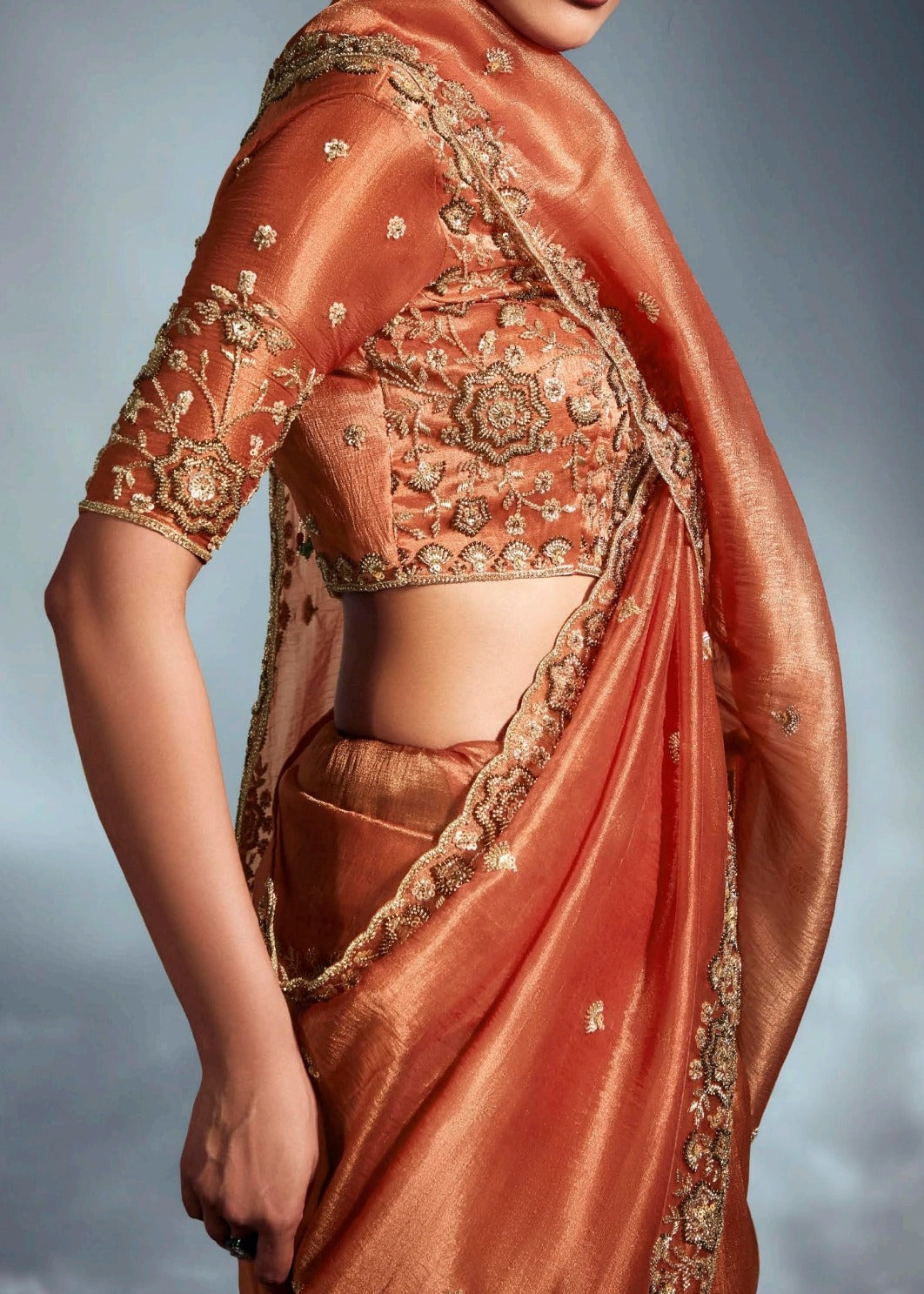 Luxury rust orange tissue silk saree with traditional hand embroidery for festive occasions.