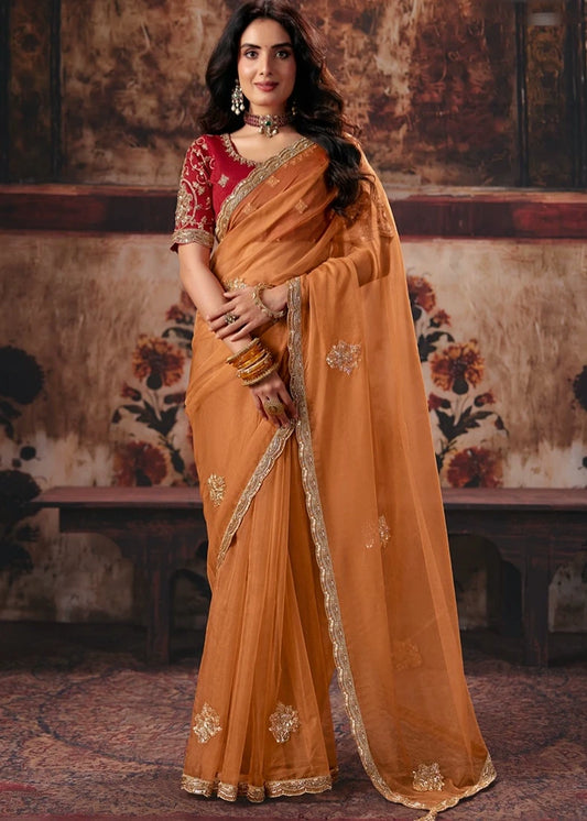 A woman modeling a traditional Indian organza silk saree in a warm orange color with gold floral embroidery and a red embroidered blouse, featuring nalki work, beadwork, sequins florals, dori work, zari work and zardozi.