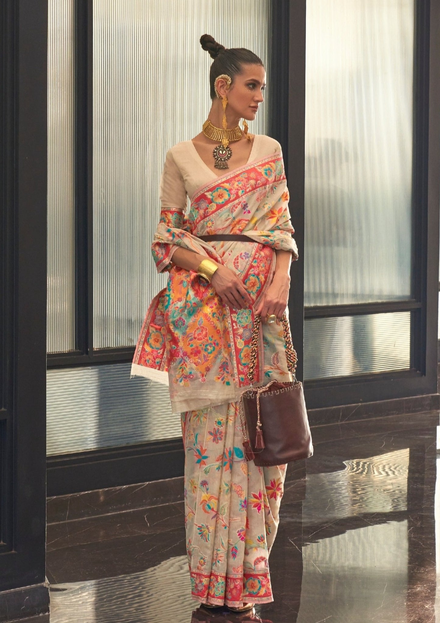woman standing in white kashmiri silk saree holding brown leather satchel bag in left hand