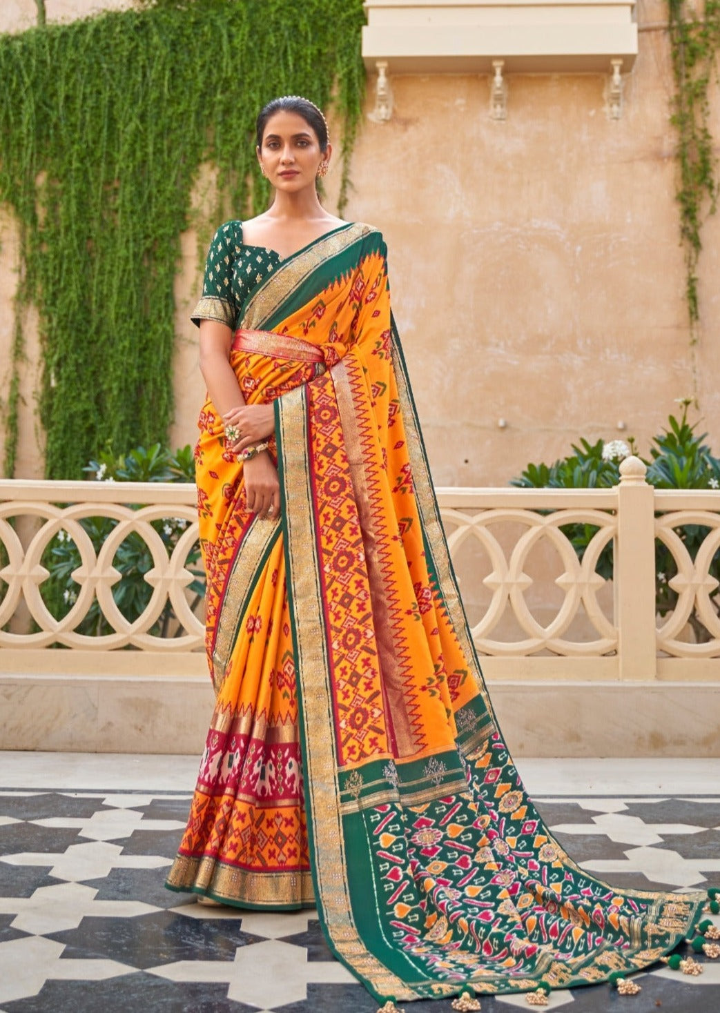 woman standing in verandah wearing yellow patola saree & green blouse