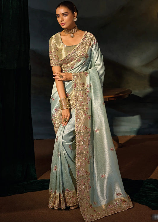 A woman in pastel pista green saree with gold zari embroidery, floral motifs, tree designs paired with a gold embroidered blouse and artisanal borders.