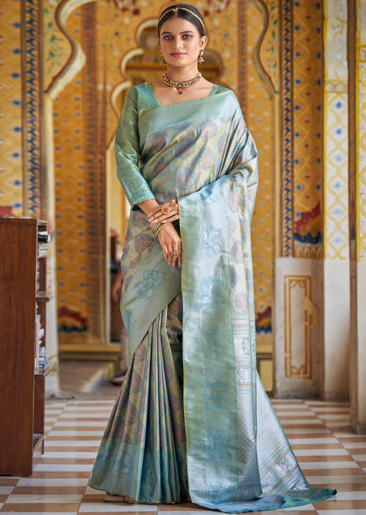 Woman standing in light sky blue Kanchipuram saree with intricate gold zari weaving floral motifs and jaal pattern all over. It has a matching blouse with sleeve border and a rich pallu.