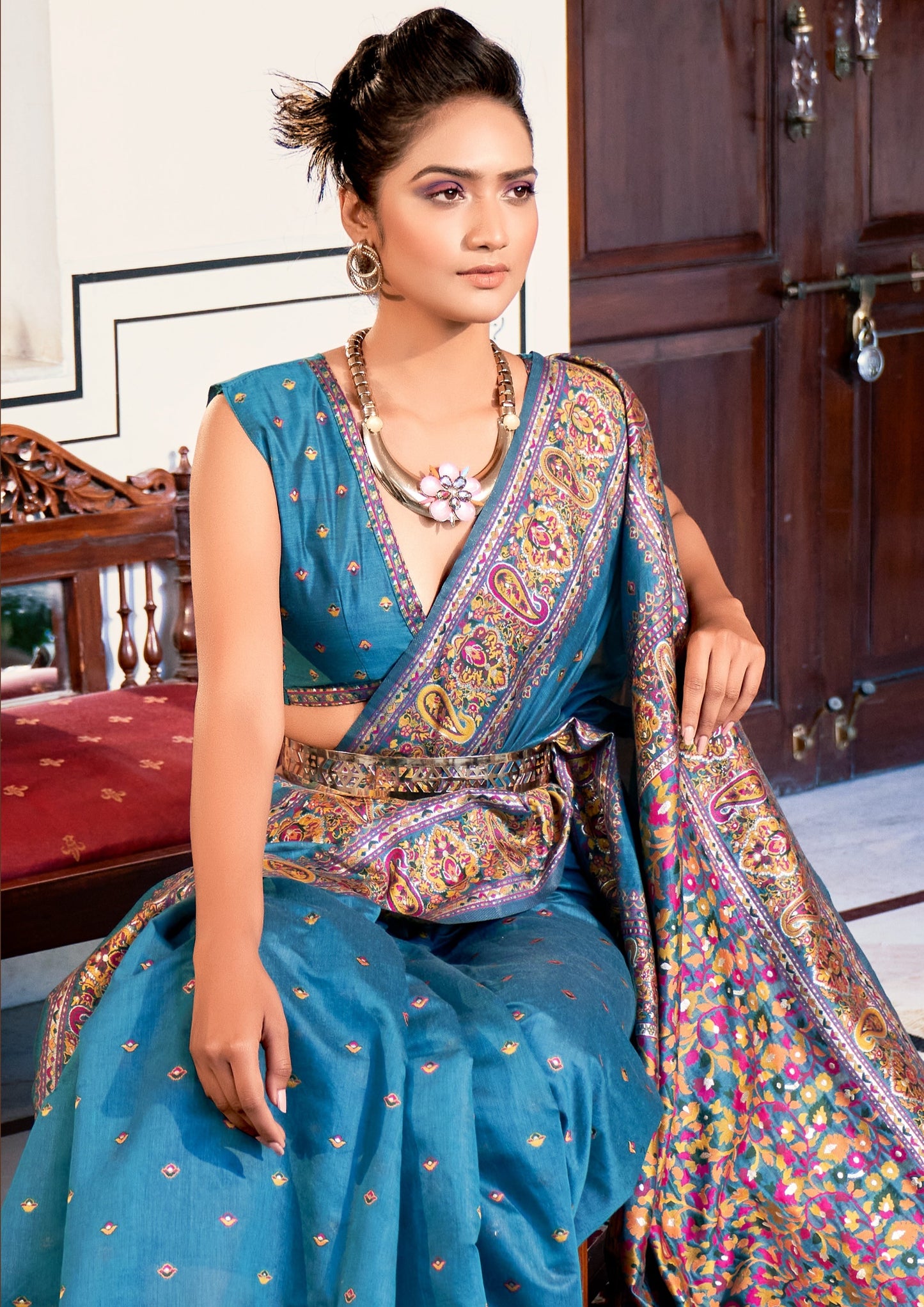 woman sitting in Pure Kashmiri Pashmina Silk Embroidered blue Handloom Saree in front of wooden door with red matress