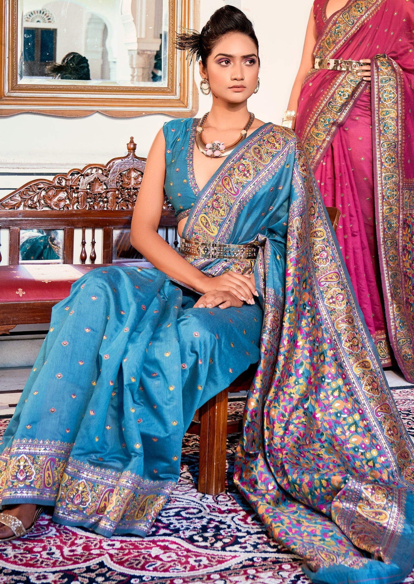 woman sitting in Pure Kashmiri Pashmina Silk Embroidered blue Handloom Saree in front of wooden bench style sofa with red matress