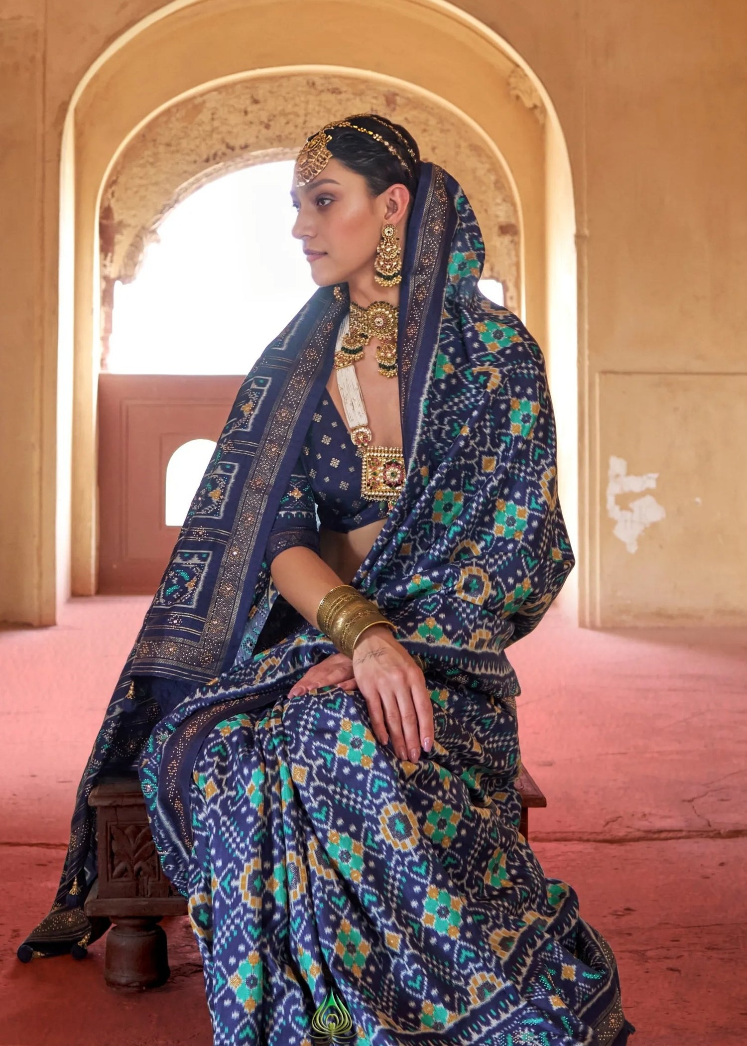 Close-up of intricate patola motifs on navy blue silk saree on indian model wearing traditional gold jewelry.