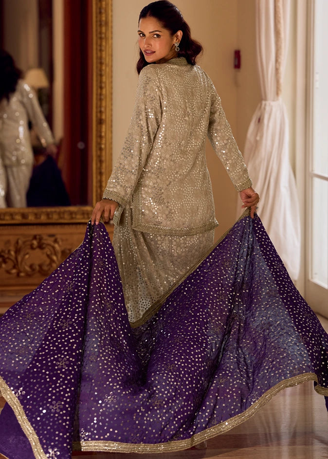 A woman modeling a traditional Indian outfit in usa with a beige sequined kurta top and a flowing violet purple dupatta decorated with gold mirror work, set in an elegant wedding hall.
