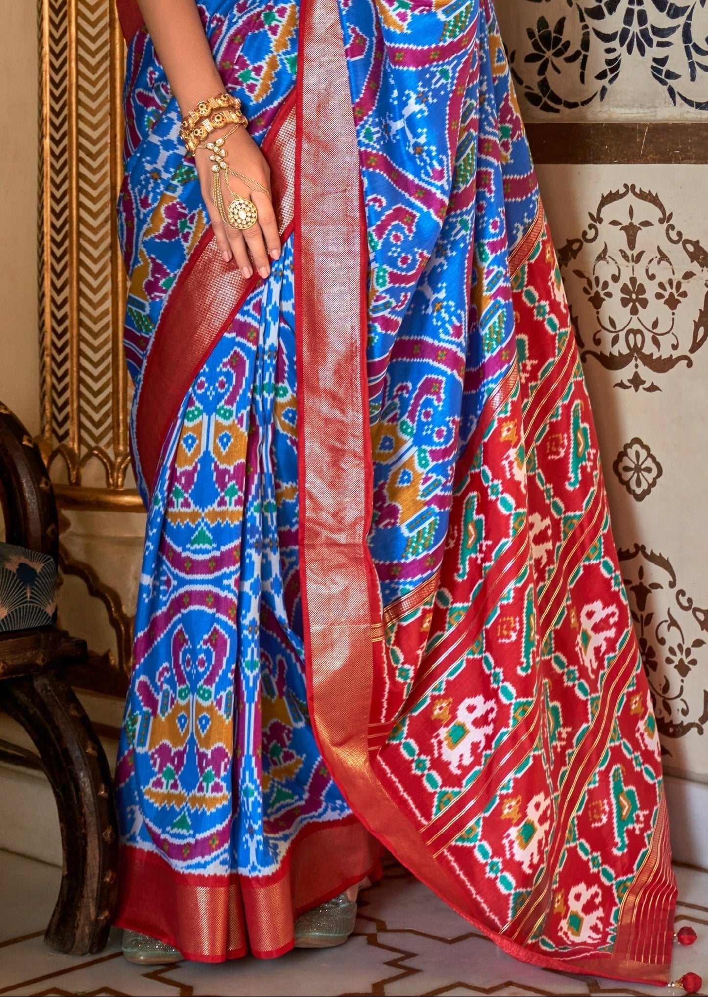 Colorful traditional patola saree with blue and red patterns on a decorative background.