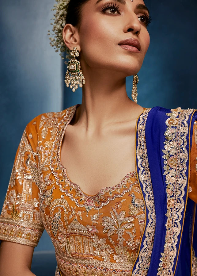 Woman wearing traditional embroidered royal blue saree and orange blouse with traditional jewelry.
