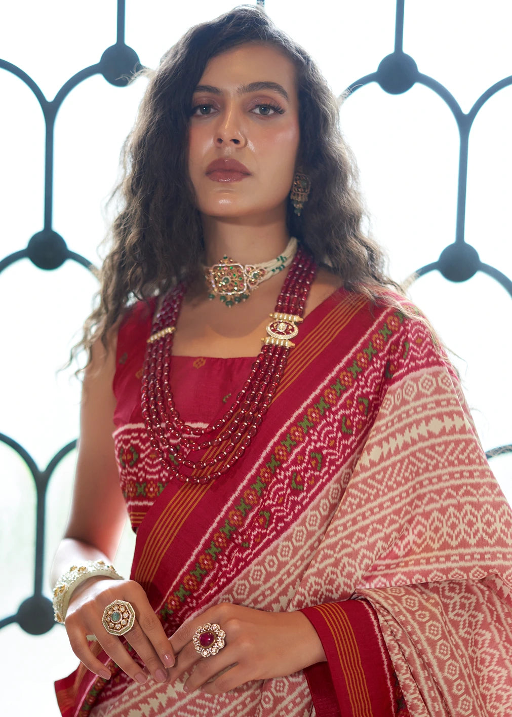 Close-up of a white Patola silk saree with intricate peach and red geometric patterns and a solid red border.