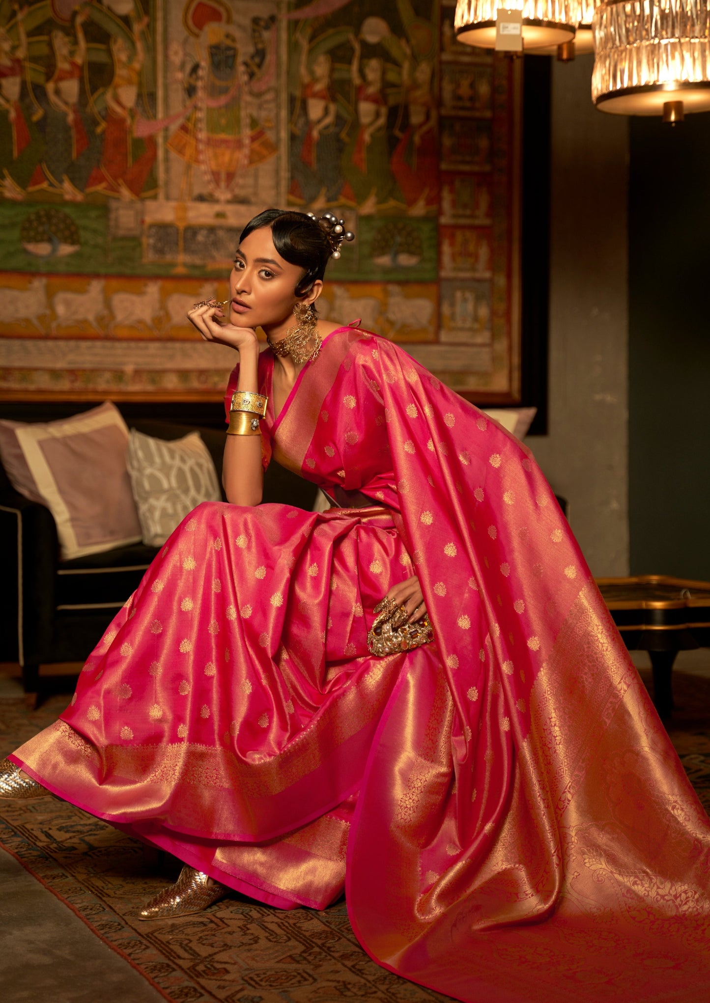 woman sitting in front of black sofa wearing banarasi Silk red Handloom Bridal Saree holding golden purse in left hand