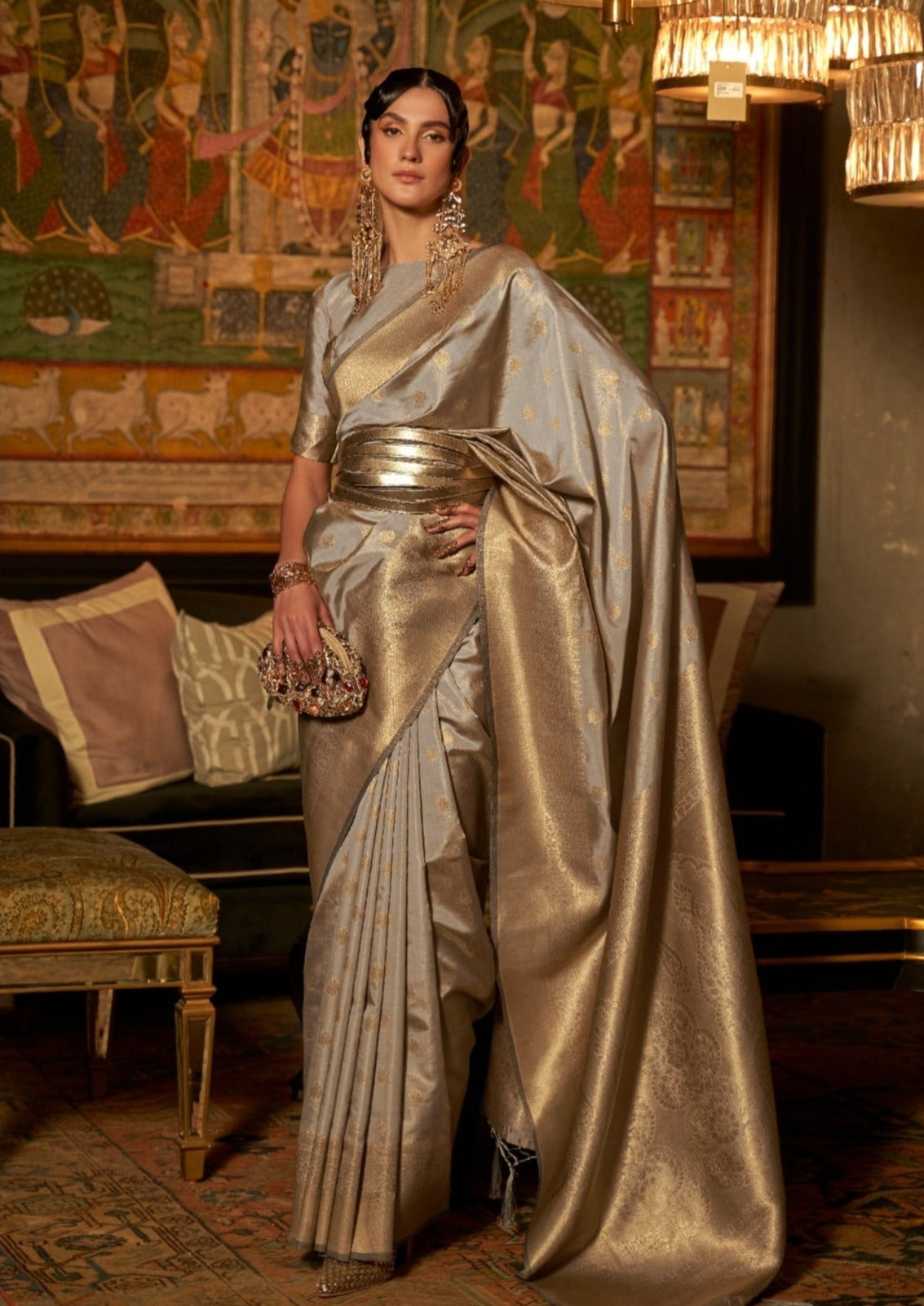 woman standing in front of black sofa wearing banarasi Silk silver Handloom Bridal Saree holding golden purse in right hand