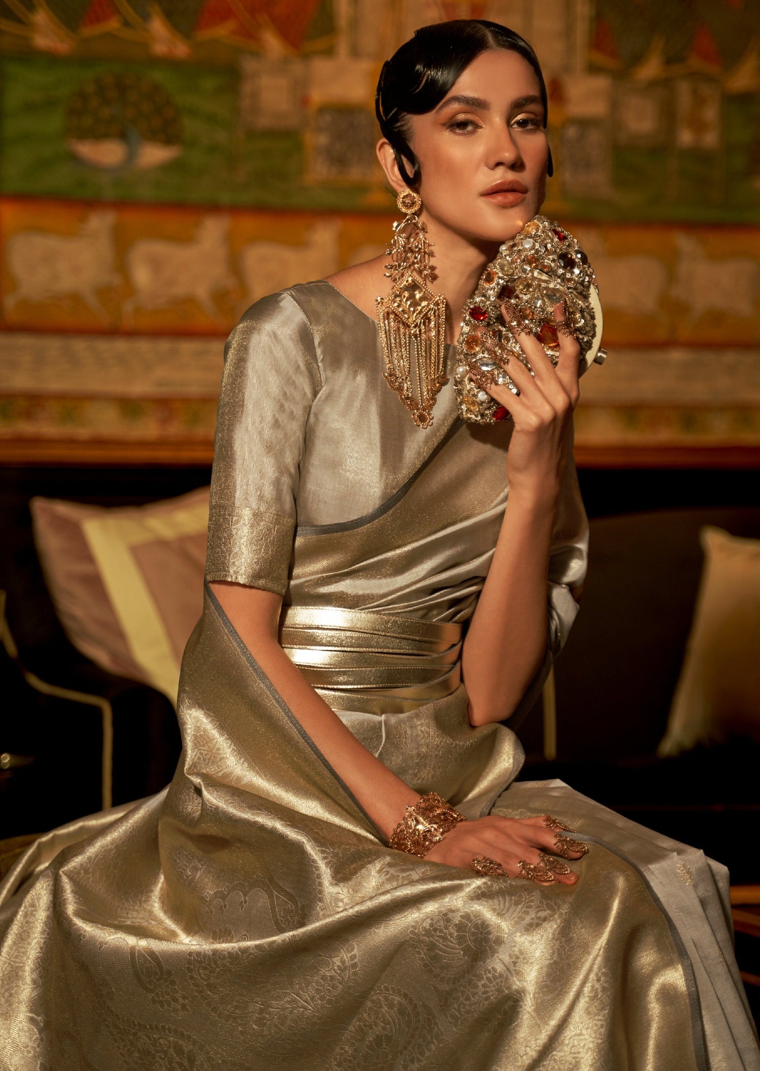 woman standing in front of black sofa wearing banarasi Silk silver Handloom Bridal Saree holding golden purse in left hand