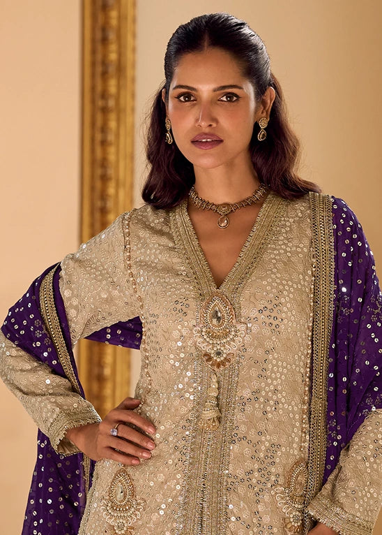 A woman modeling a traditional south asian indian co ord set outfit featuring a heavily embellished beige kurta with silver mirror work, sequins embroidery, stone work and a deep violet purple dupatta draped over her shoulders.