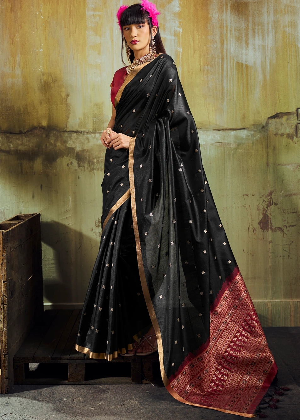 Woman wearing a black banarasi silk saree with gold zari border and red blouse against a textured golden wall; for online shopping in norway.