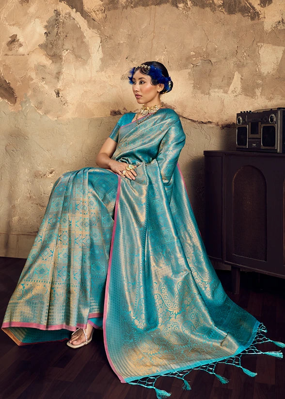 Seated woman draped in a premium turquoise blue and gold Banarasi silk saree for wedding wear.