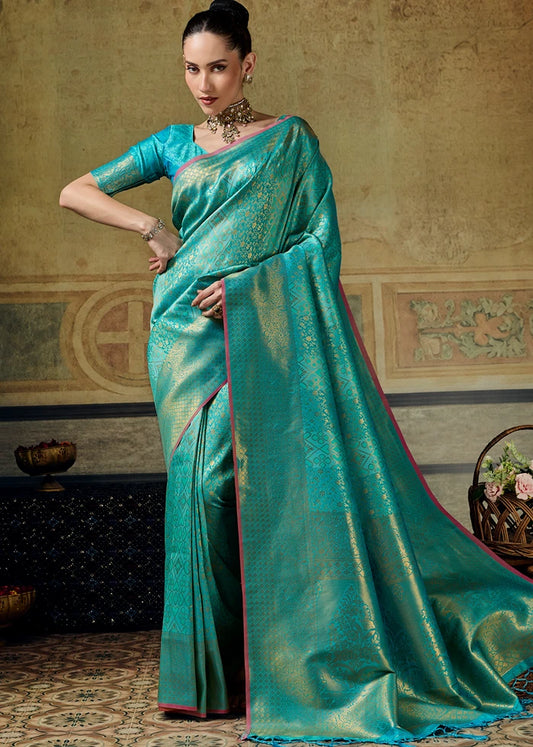 A woman models a royal turquoise blue kanjivaram silk saree with gold zari embroidery and heavy border, paired with a matching blouse.