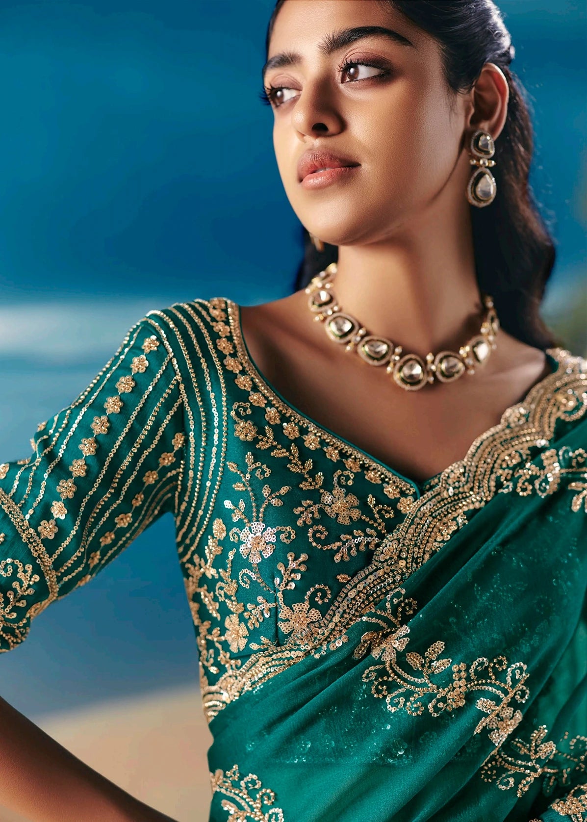 Woman in festive wear emerald green silk saree with golden embroidery against a blurred natural background.