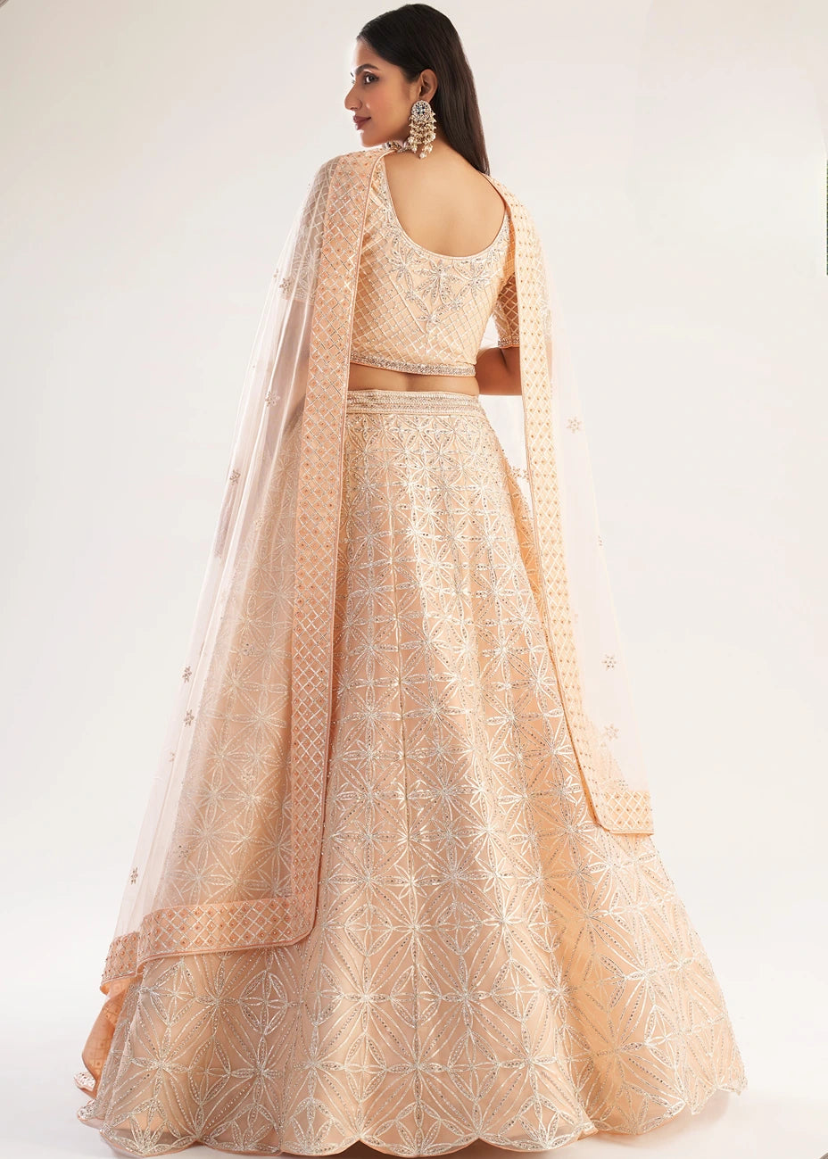 A woman modeling a peach-beige gota patti embroidered lehenga choli set with a sheer net dupatta, shown from the back against a plain white studio background.