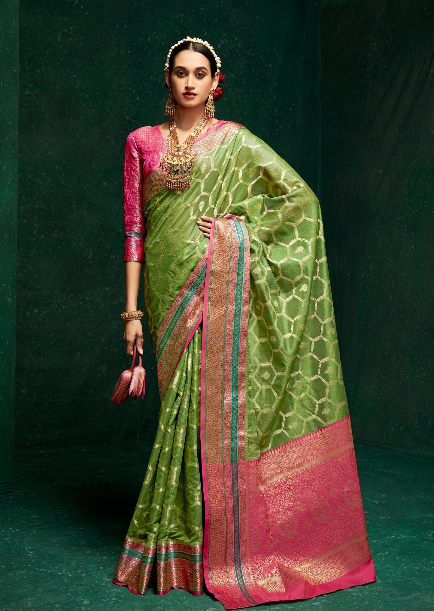 Woman standing in green banarasi silk saree holding a pink lotus in right hand