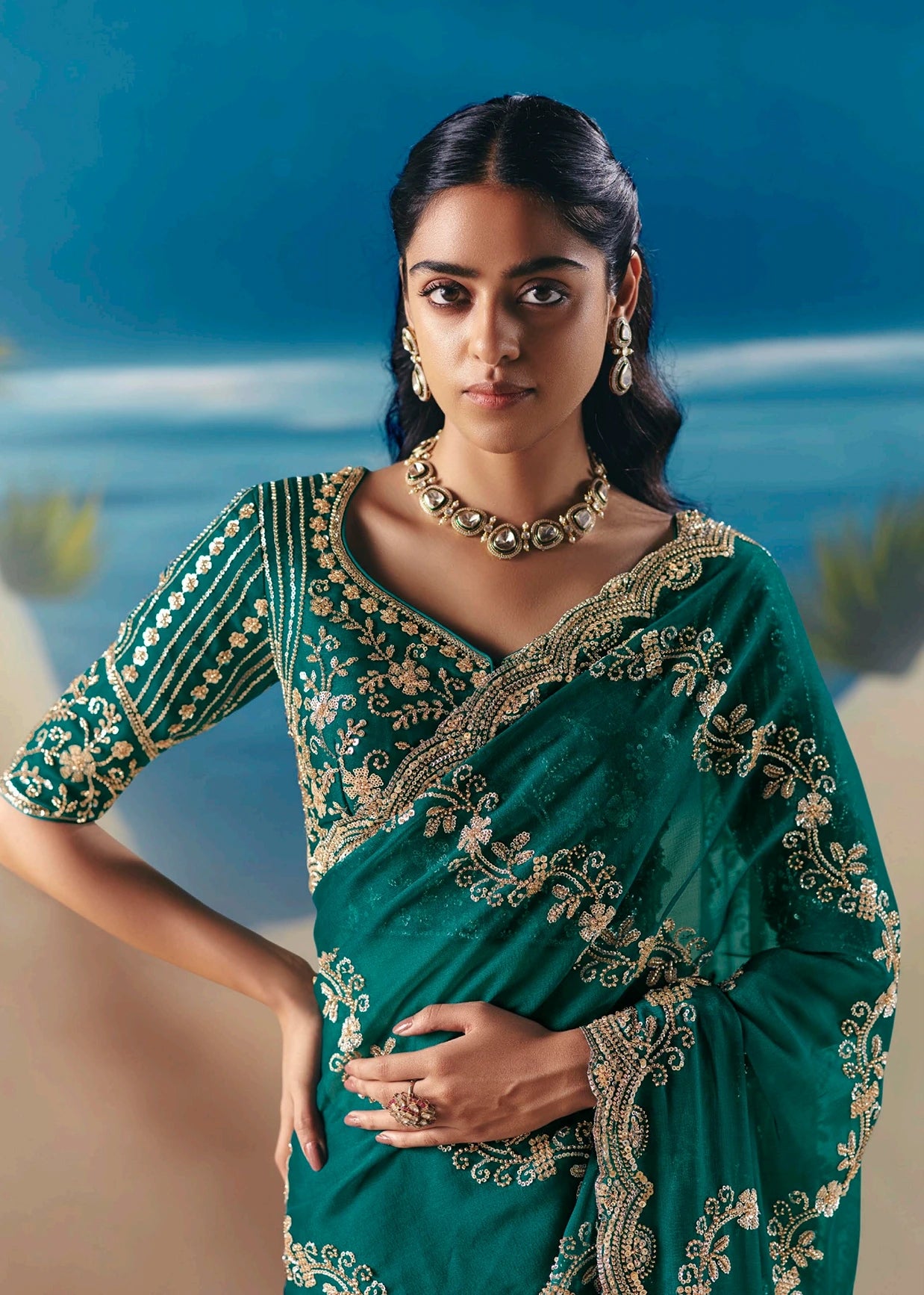 Woman in a dark green organza tissue silk bridal saree with gold embroidery and traditional Indian jewellery.