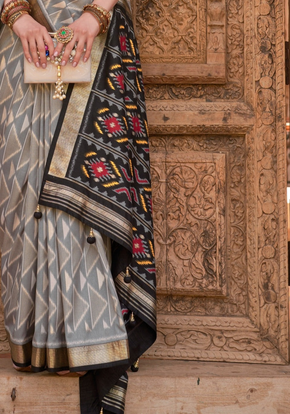 Grey patola saree design online shopping, featuring black pallu with red and yellow traditional ikkat motifs.