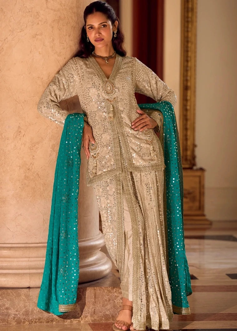 A woman models a traditional Indian outfit in netherlands consisting of a heavily embellished beige kurta and matching dhoti skirt with a bright turquoise blue dupatta, posed in front of a warm-toned marble column.