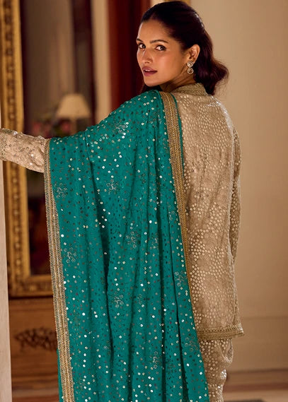 A woman wearing a traditional Indian outfit in netherlands with a teal blue sequined dupatta and a beige embroidered georgette kurta top, photographed indoors against a warm-toned background.