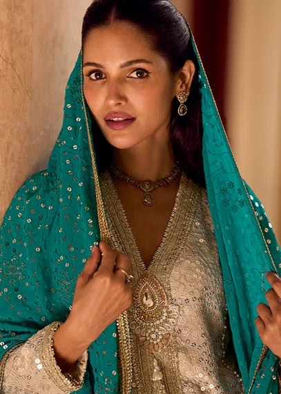 A woman wearing traditional Indian wedding attire in netherlands, featuring a turquoise blue embroidered dupatta draped over her shoulders and a beige sequined embroidered kurta. She is adorned with gold jewelry, including earrings and a necklace.