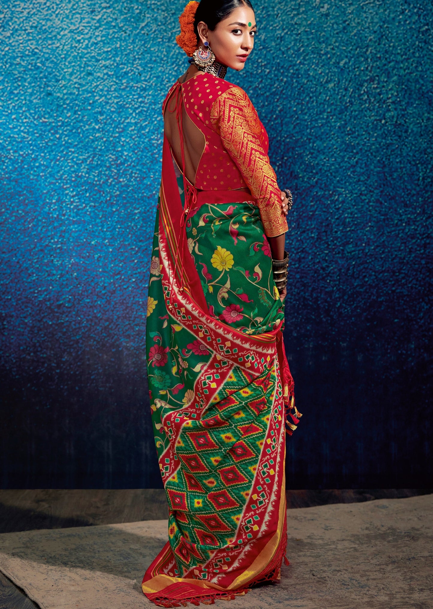 Woman with green bindi standing in Green Kalamkari Patola Fusion Saree in front of a blue wall