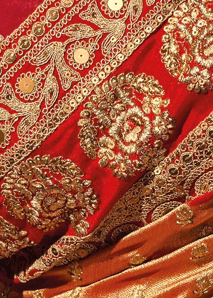 Close-up detail of the heavy gold zari thread embroidery and micro-fine sequins work on red border of a premium rust orange silk saree.