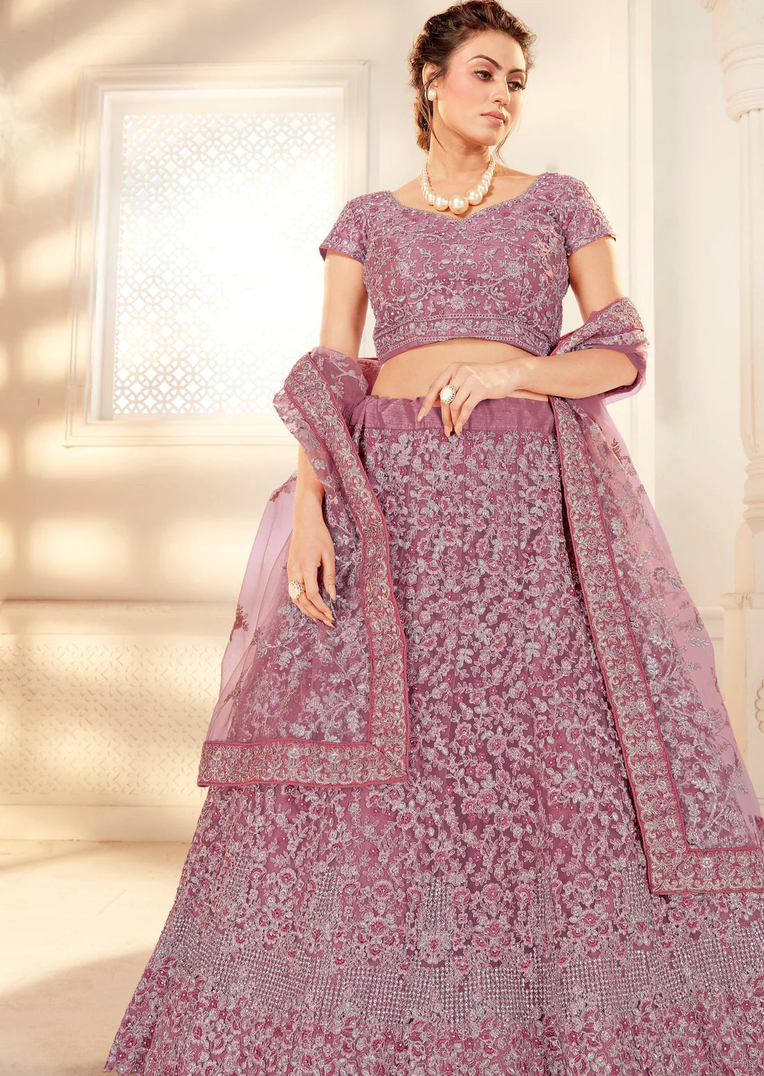 woman standing in purple lehenga with heavy embroidery work in front of a white wall