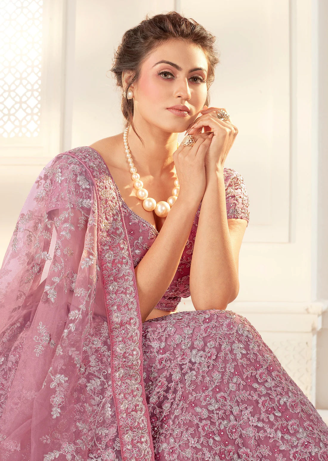 woman wearing pearl necklace posing in purple lehenga with heavy embroidery work in front of a white wall