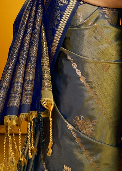 A close-up of a draped military green saree with a deep navy blue border and a shimmering body, decorated with intricate gold zari embroidery and tassels.