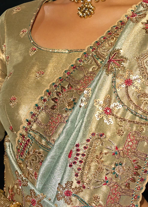 Close-up of a traditional embroidered kanjivaram saree with a light green body and a gold blouse featuring mirror work snd intricate floral paisley embroidery in gold, red, and green.