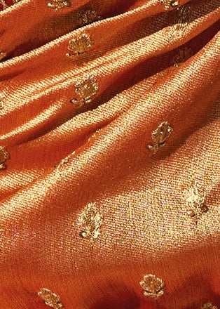 Close-up of draped orange kanjivaram silk saree fabric with small metallic gold floral motifs with sequins embroidery woven throughout.