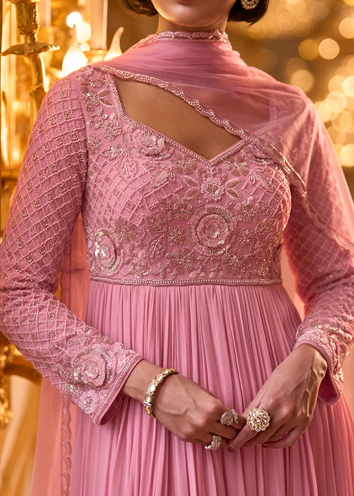 A close-up of a woman wearing a pink traditional embroidered anarkali with a sheer dupatta, long embellished sleeves.