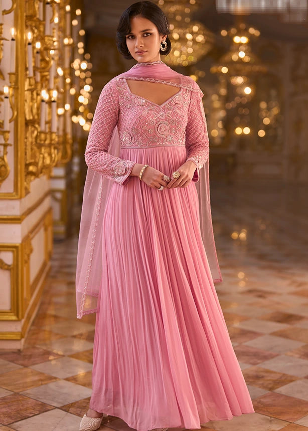 Woman modeling a pastel pink georgette anarkali gown with an embroidered bodice, long sleeves, and net dupatta.