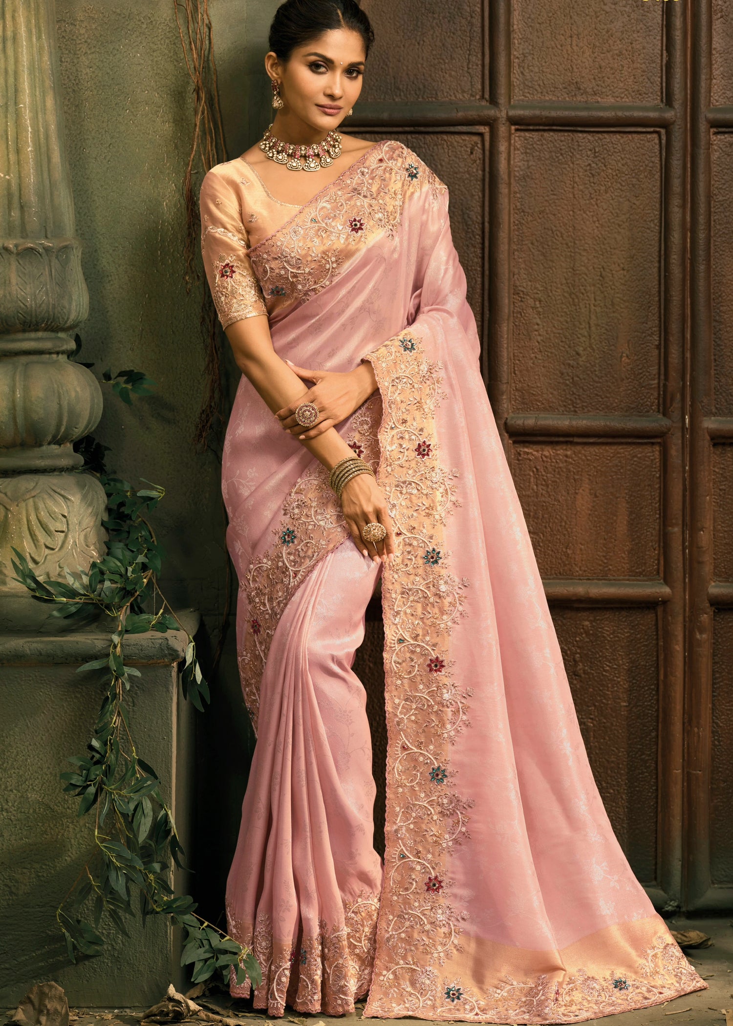 Woman wearing a pastel pink and golden kanjivaram silk saree with intricate embroidery made with pearls, zari, zardozi, stone work and dabka.