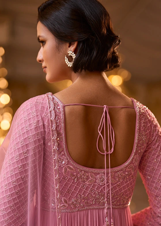 A woman shown from the back wearing a pink embellished traditional anarkali outfit with a deep open back and tie latkan detail.