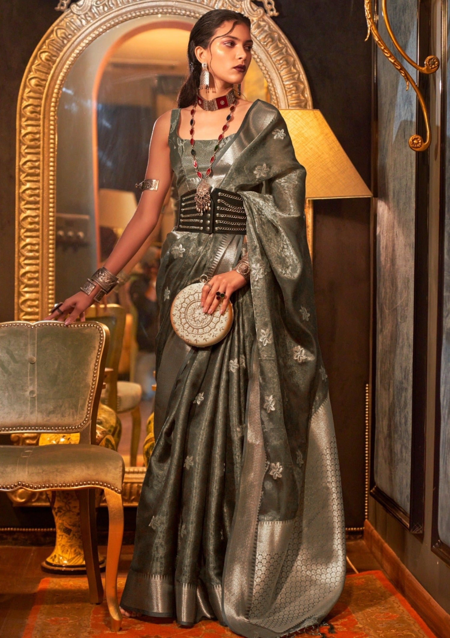 woman standing in black colour banarasi organza saree in front of a black wall having golden frame mirror