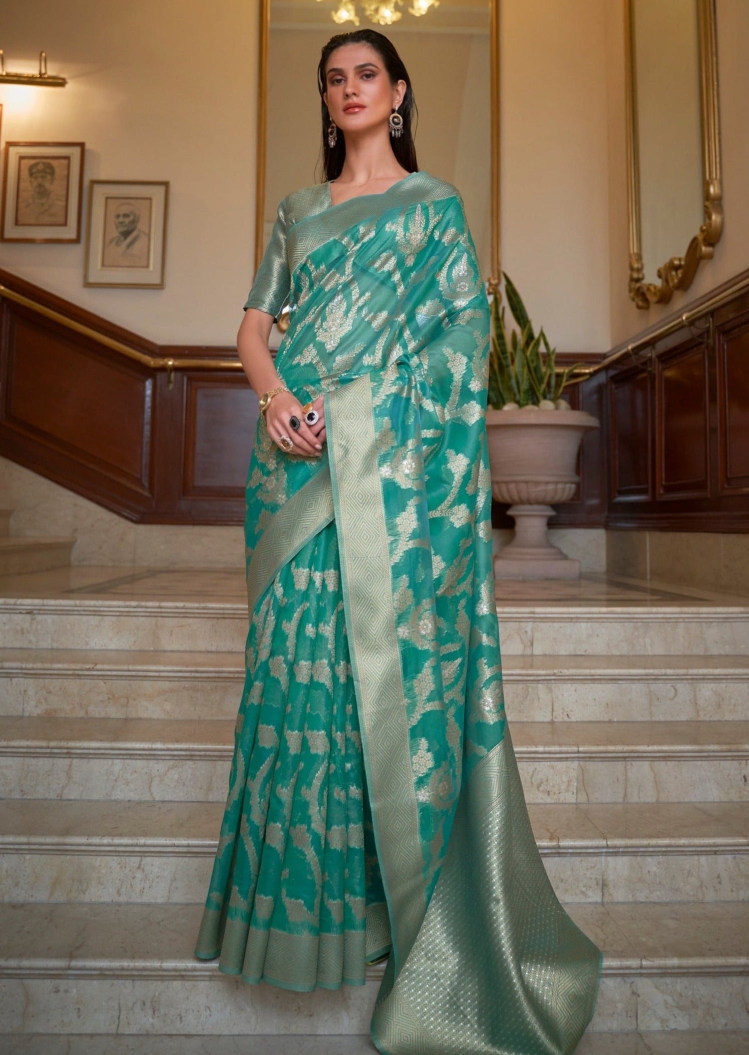 Woman in green color Banarasi Organza saree standing on white marble stairs