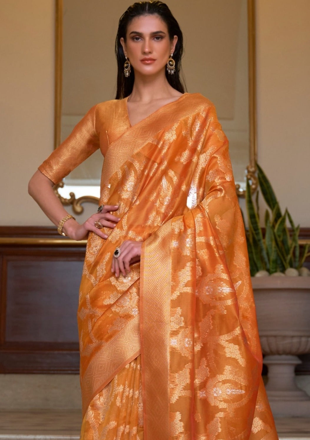 woman in orange colour organza saree with right hand on waist