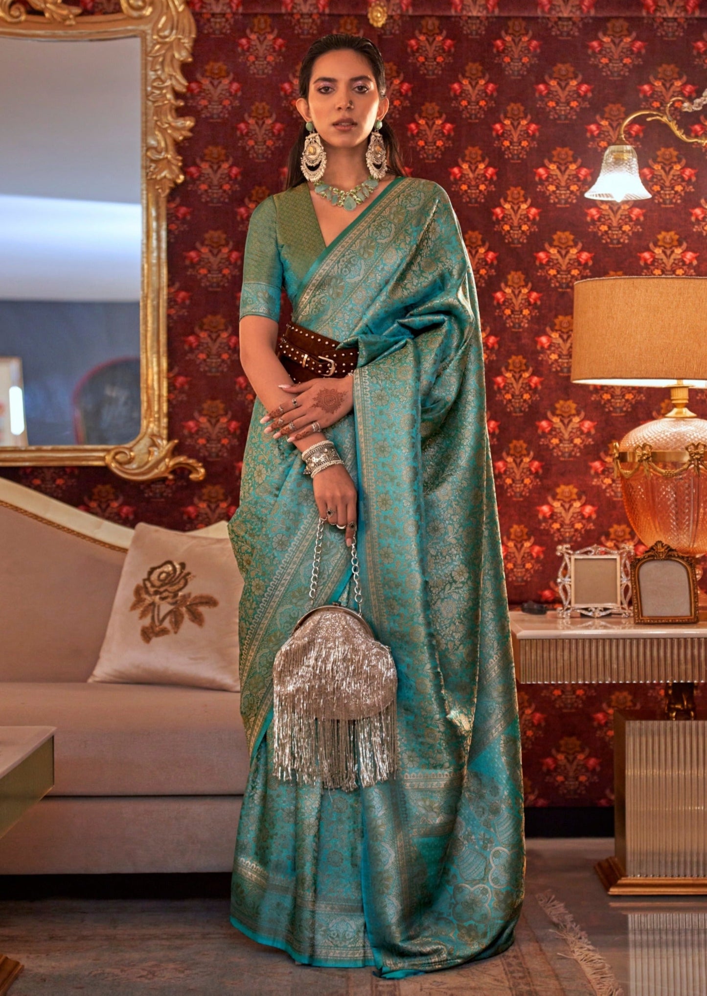 woman standing in Banarasi Silk blue Handloom Bridal Saree in front of a white sofa holding silver purse in right hand
