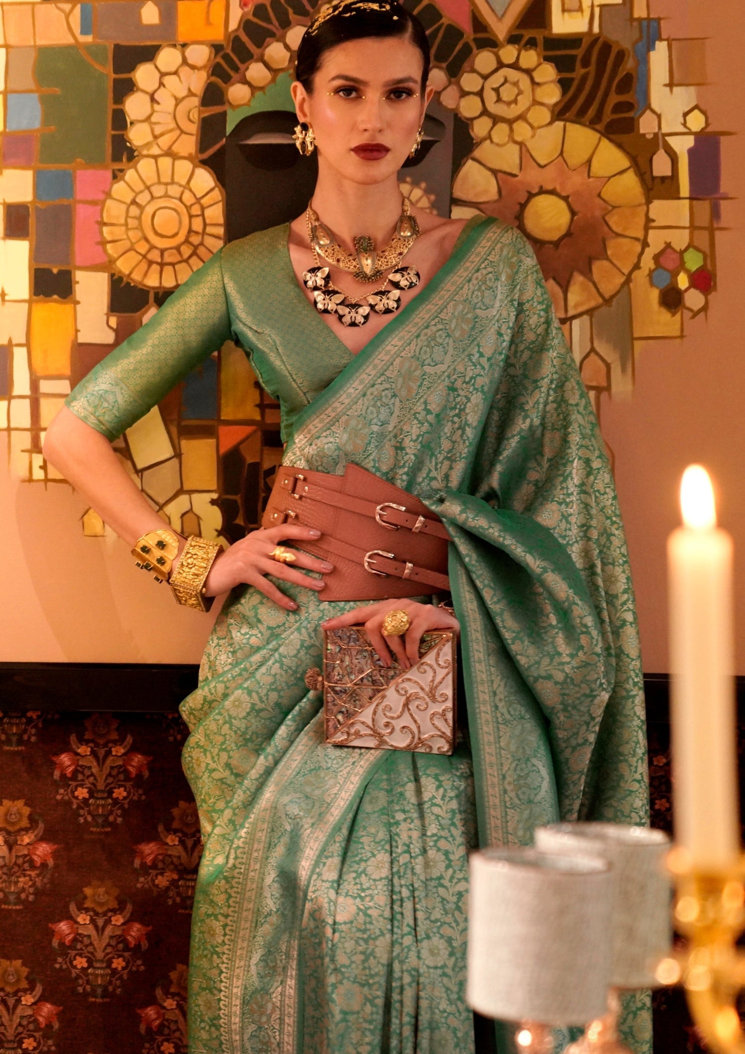 woman in green colour banarasi silk saree standing against a wall holding right hand on waist