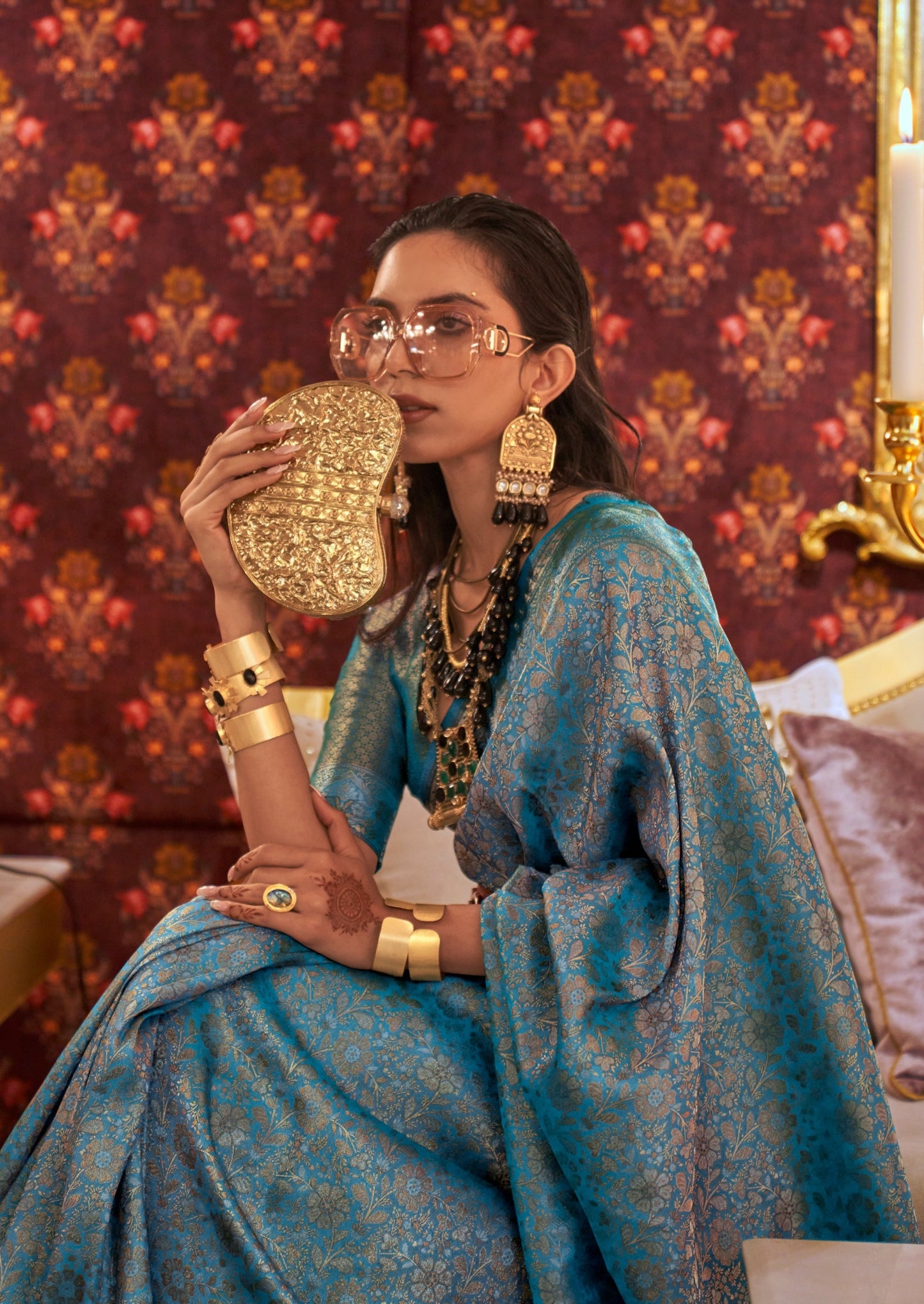 woman wearing light pink sunglasses sitting in Banarasi Silk Peacock Blue saree ang gold jewelry