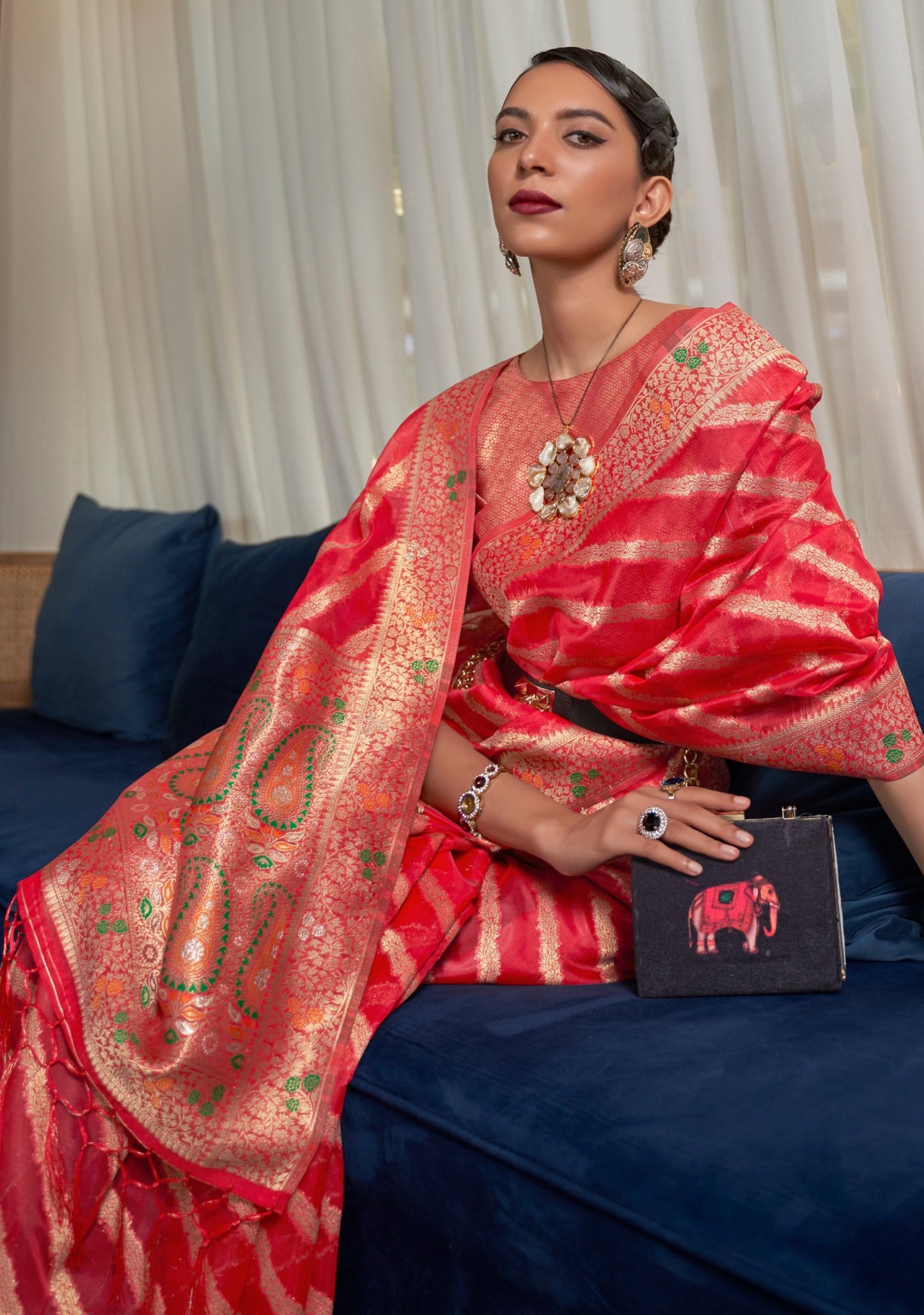 woman sitting in red handloom organza saree with meenakari pallu having paisley motifs.