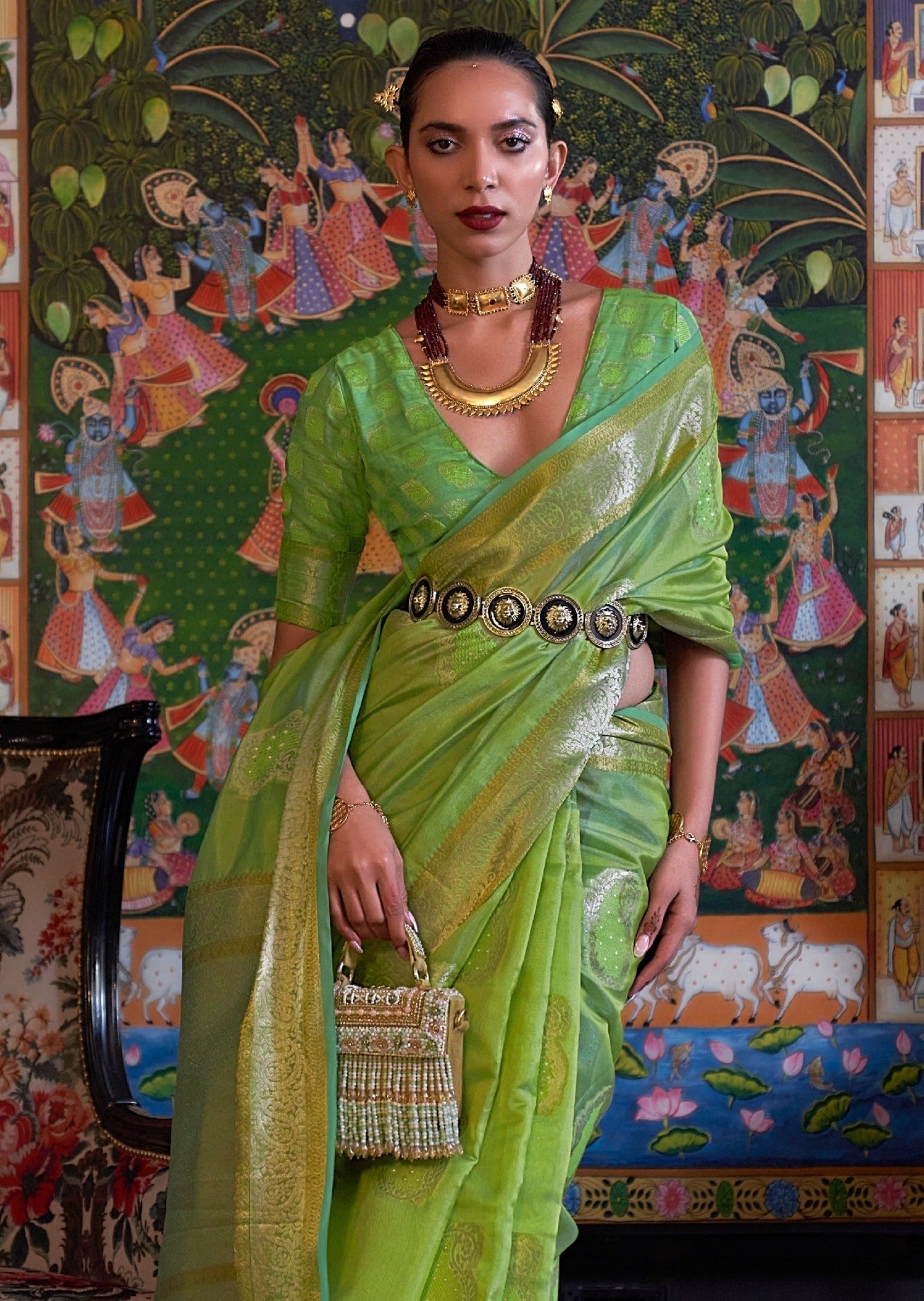 woman wearing light green handloom banarasi organza saree holding a fancy bag in her right hand