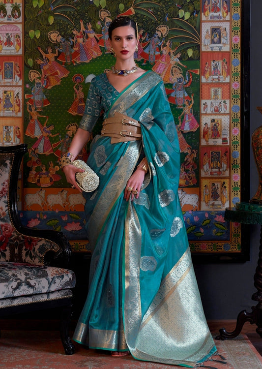 woman standing in blue color banarasi organza saree in front of a big vertical pichwai painting