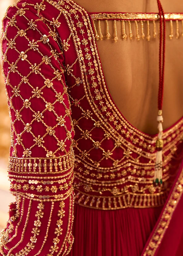 Close-up of a red and gold heavily embellished traditional anarkali outfit, showing intricate gold embroidery, beadwork, and a deep open back on a woman.