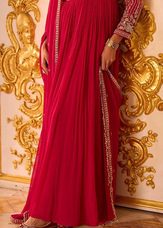 A woman wearing a long red pleated anarkali gown with gold embroidered sleeves and a matching net dupatta.